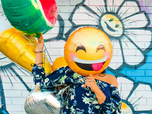 person holding foil smile balloon in front of her face